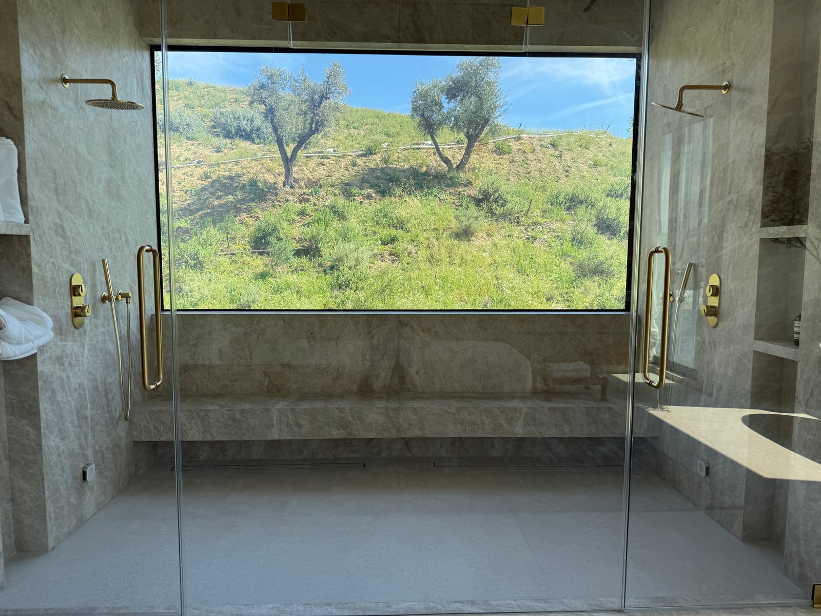 Switchable smart glass window in a marble bathroom, shown clear with a green hillside view